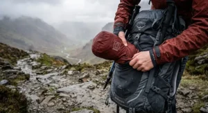 A lightweight, packable hardshell jacket being stowed into a rucksack, ideal for changeable British weather.