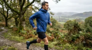 Side profile of a runner wearing a blue men's waterproof running jacket with zipped pockets for secure storage.