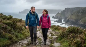 A couple wearing their chosen best walking jacket models while enjoying a rainy day hike on a coastal path.