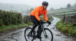 Cyclist wearing a fluorescent orange hi-vis cycling rain jacket riding through heavy British drizzle