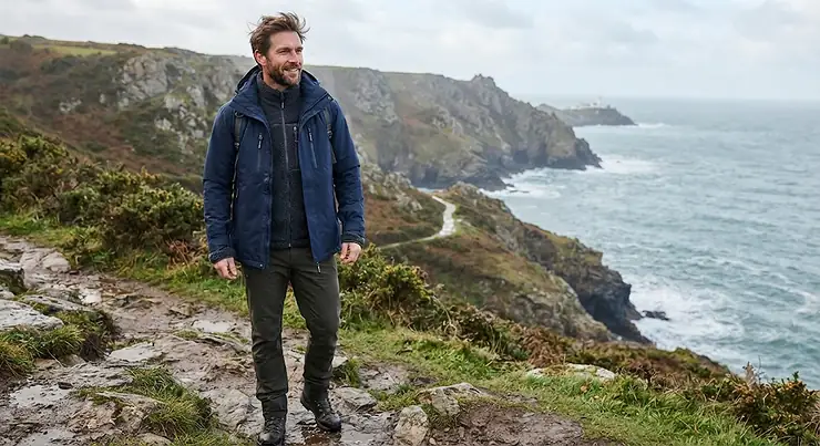 A man wearing a navy blue mens 3 in 1 jacket, featuring a detachable fleece liner suitable for British weather.