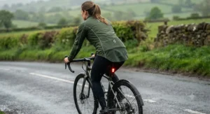 Rear view showing the drop-tail hem of a tailored womens cycling rain jacket protecting against road spray from wet tarmac.