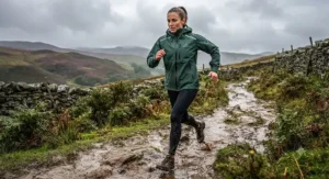Trail runner navigating a muddy British path in a durable weather-resistant womens running rain jacket