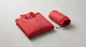 Bright red mens golf waterproof jacket folded neatly beside its matching waterproof pouch for easy bag storage