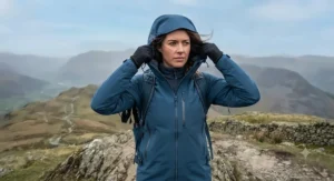 Hiker adjusting the adjustable hood on her windproof womens outdoor jacket on a windy peak