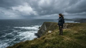 A person braving the wind in the best wax jacket overlooking a dramatic British coastline and stormy sea
