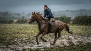 A rider wearing an equestrian waterproof jacket while galloping across a muddy British field in the rain.