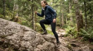 A hiker stepping over a mossy boulder, demonstrating the articulated knees of men's waterproof trousers.