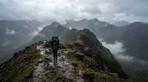 A hiker wearing men's waterproof trousers walking along a muddy ridge in the Scottish Highlands during a heavy downpour.