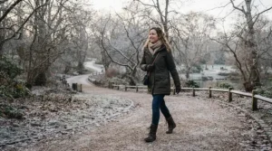 Woman wearing a stylish waterproof padded coat while walking through a frosty London park on a crisp morning